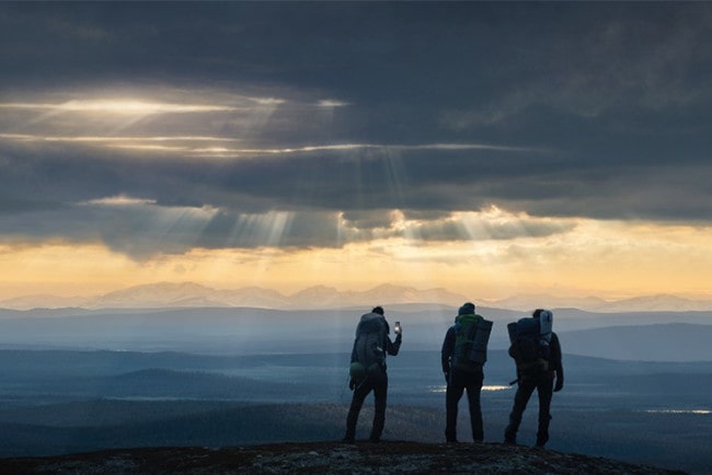Tre personer på en bergstopp där en söker mobilteckning