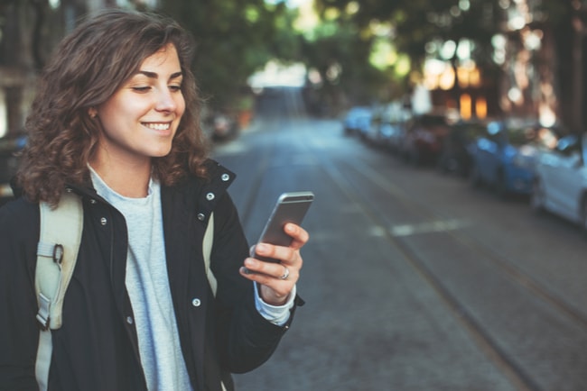 leende kvinna med mobiltelefon går på en gata